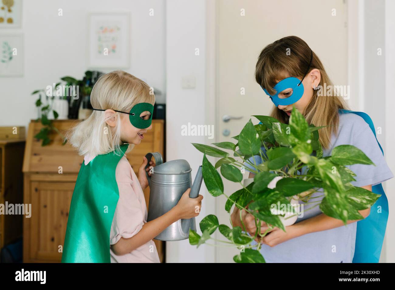 Le ragazze in costume di superdonna che tiene in vaso la pianta e l'annaffiatura possono nel paese Foto Stock