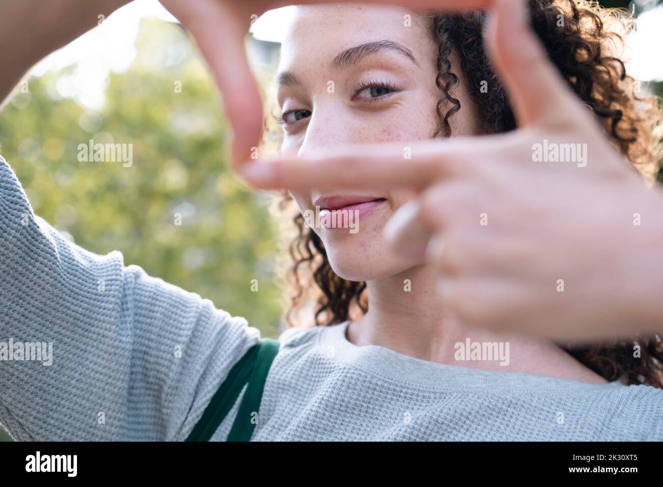 Sorridente giovane donna che guarda attraverso la cornice del dito Foto Stock