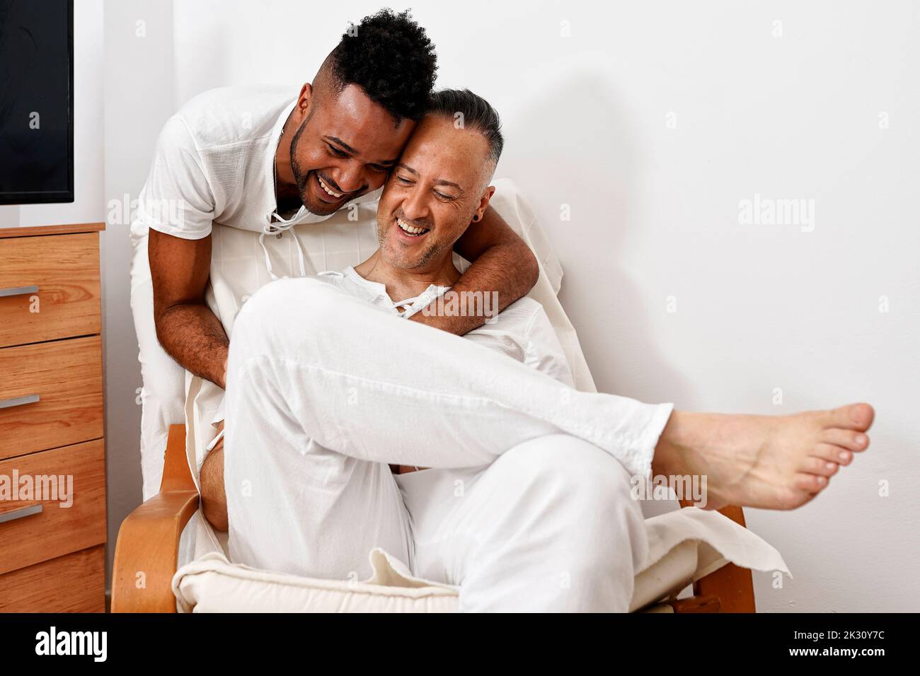 Giovane uomo allegro che abbraccia il ragazzo seduto sulla sedia Foto Stock