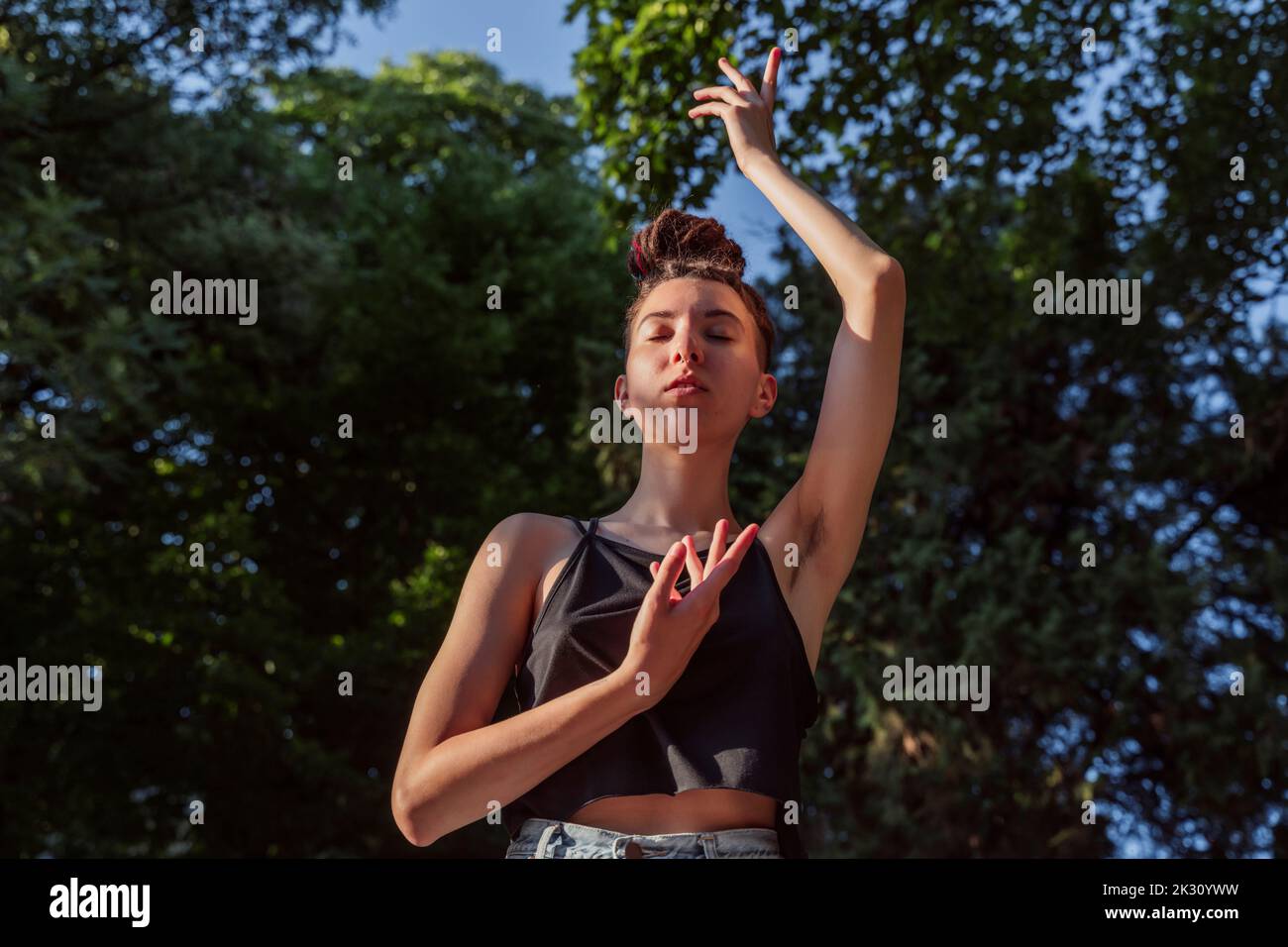 Persona non binaria gesturing con mano sollevata nella giornata di sole Foto Stock