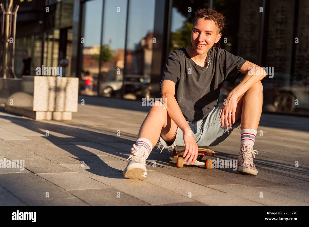 Sorridente persona non binaria seduta sullo skateboard Foto Stock