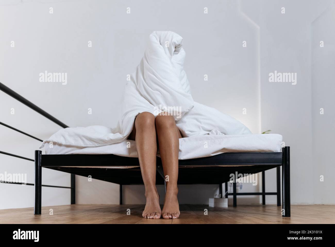 Donna depressa seduta sul bordo del letto che si nasconde in coperta Foto Stock