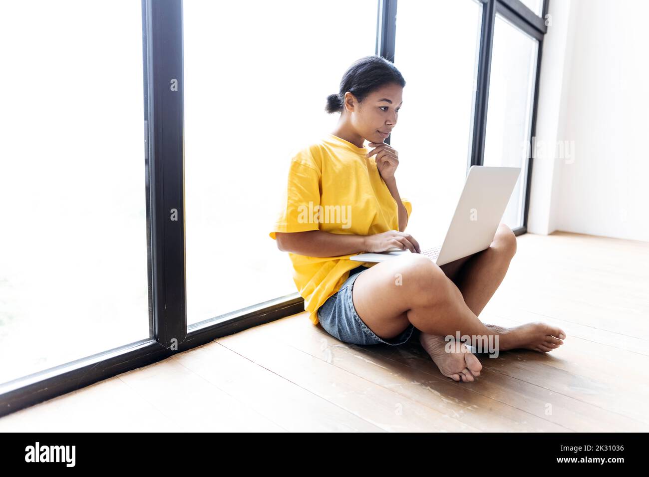 Donna che lavora su un notebook appoggiato a una finestra Foto Stock