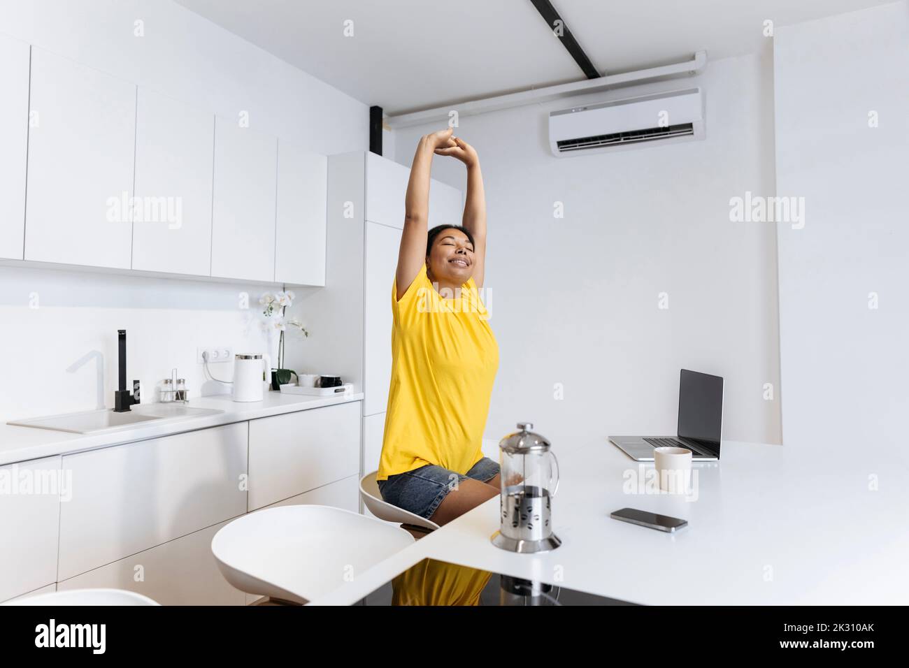 Donna felice che si allunga in cucina prendendo una pausa dal lavoro freelance Foto Stock