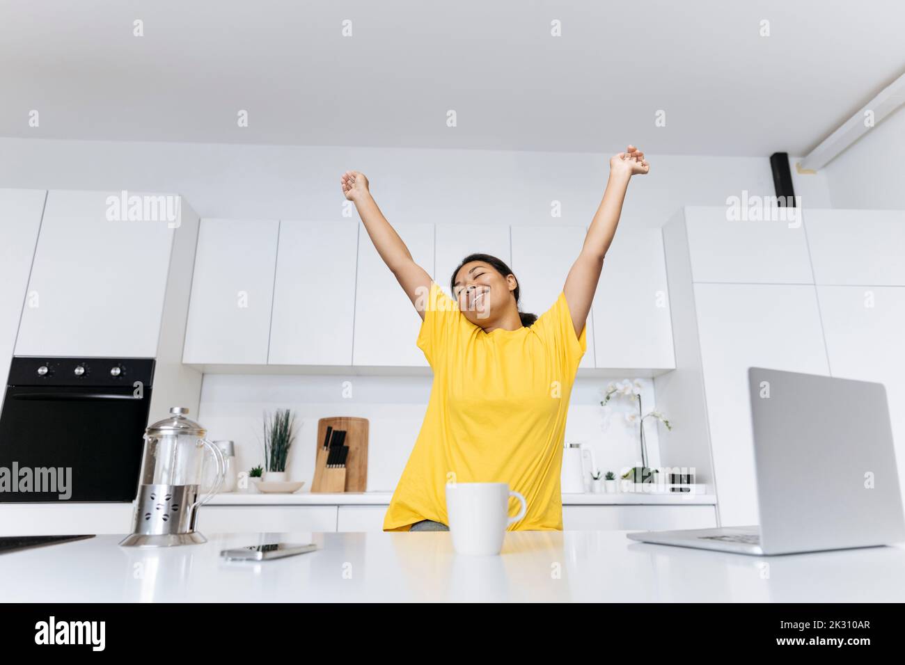 Donna felice che si allunga in cucina prendendo una pausa dal lavoro freelance Foto Stock