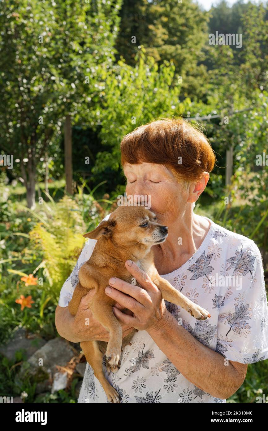 Donna anziana che bacia il cane in giardino Foto Stock