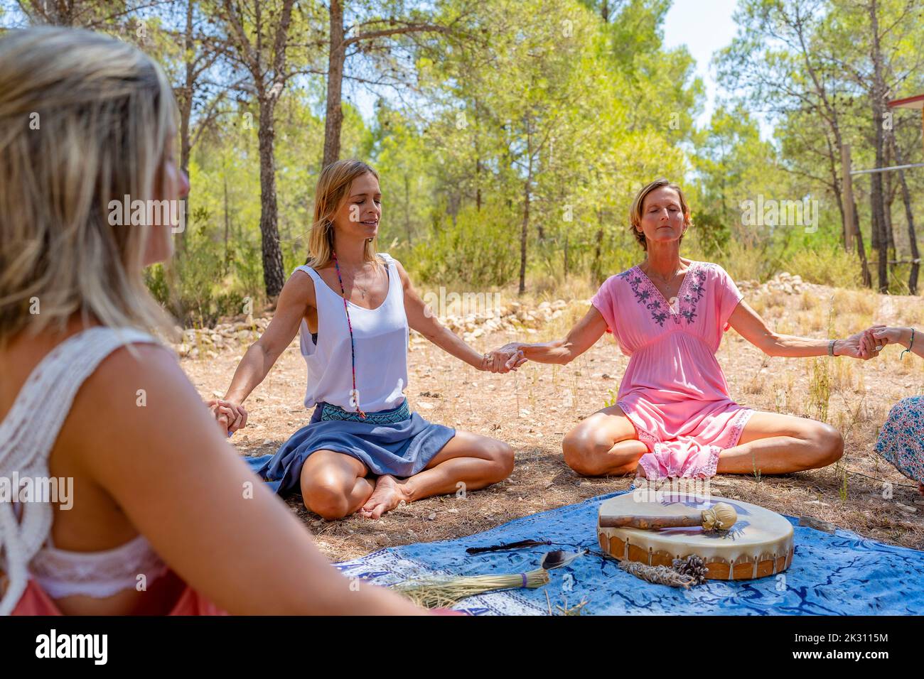 Donna matura sorridente con amici che praticano la meditazione davanti agli alberi Foto Stock