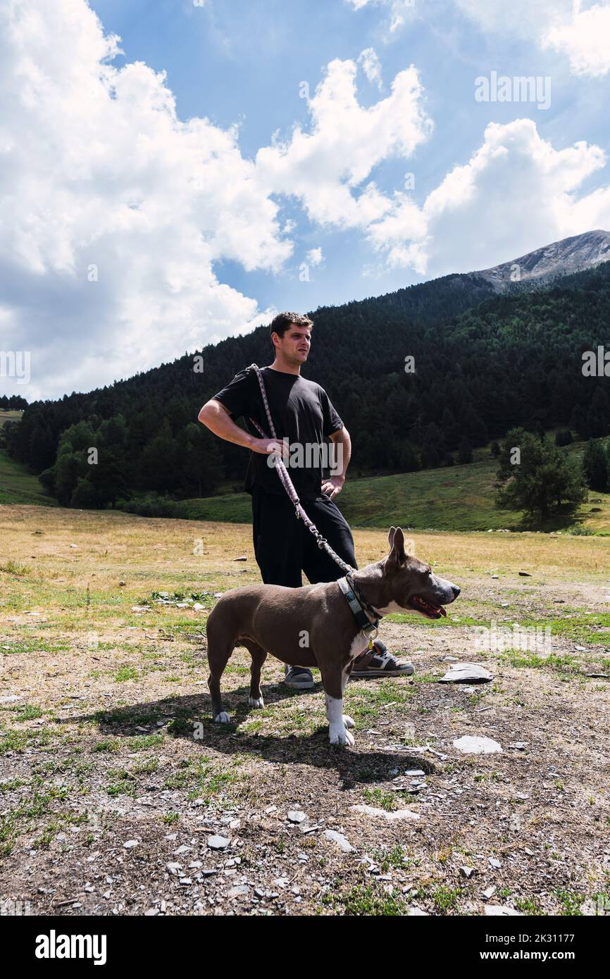 Uomo in piedi con il cane di fronte alla montagna nelle giornate di sole Foto Stock