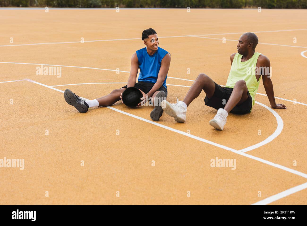 Uomo sorridente che tiene il basket parlando con il padre seduto sul campo Foto Stock