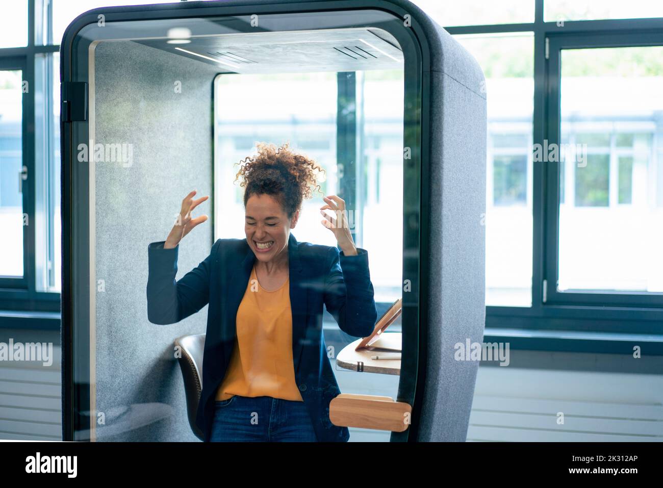 Una donna d'affari frustrata stringe i denti all'interno della cabina insonorizzata sul posto di lavoro Foto Stock