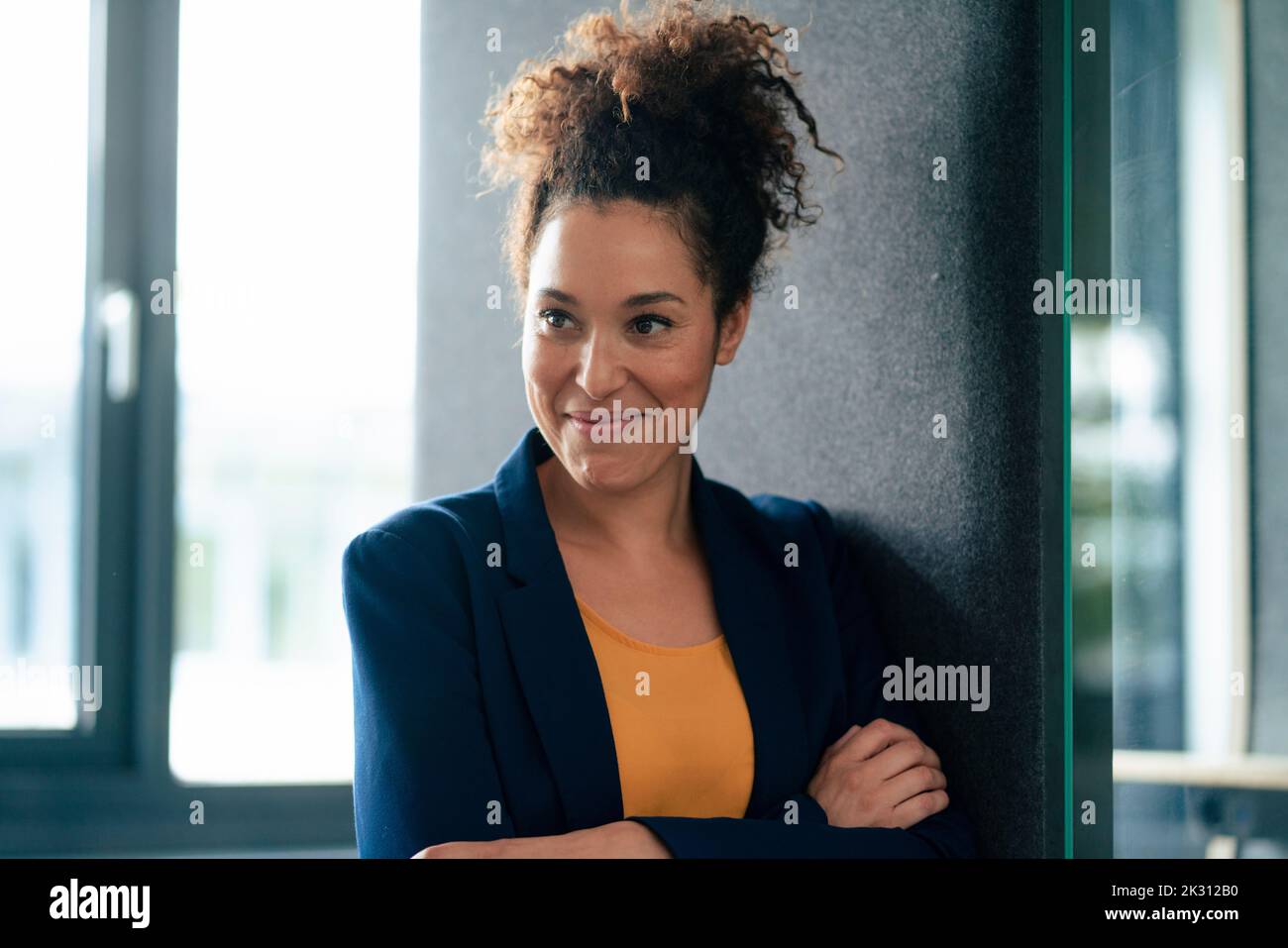 Donna d'affari sorridente con le braccia incrociate sul posto di lavoro Foto Stock