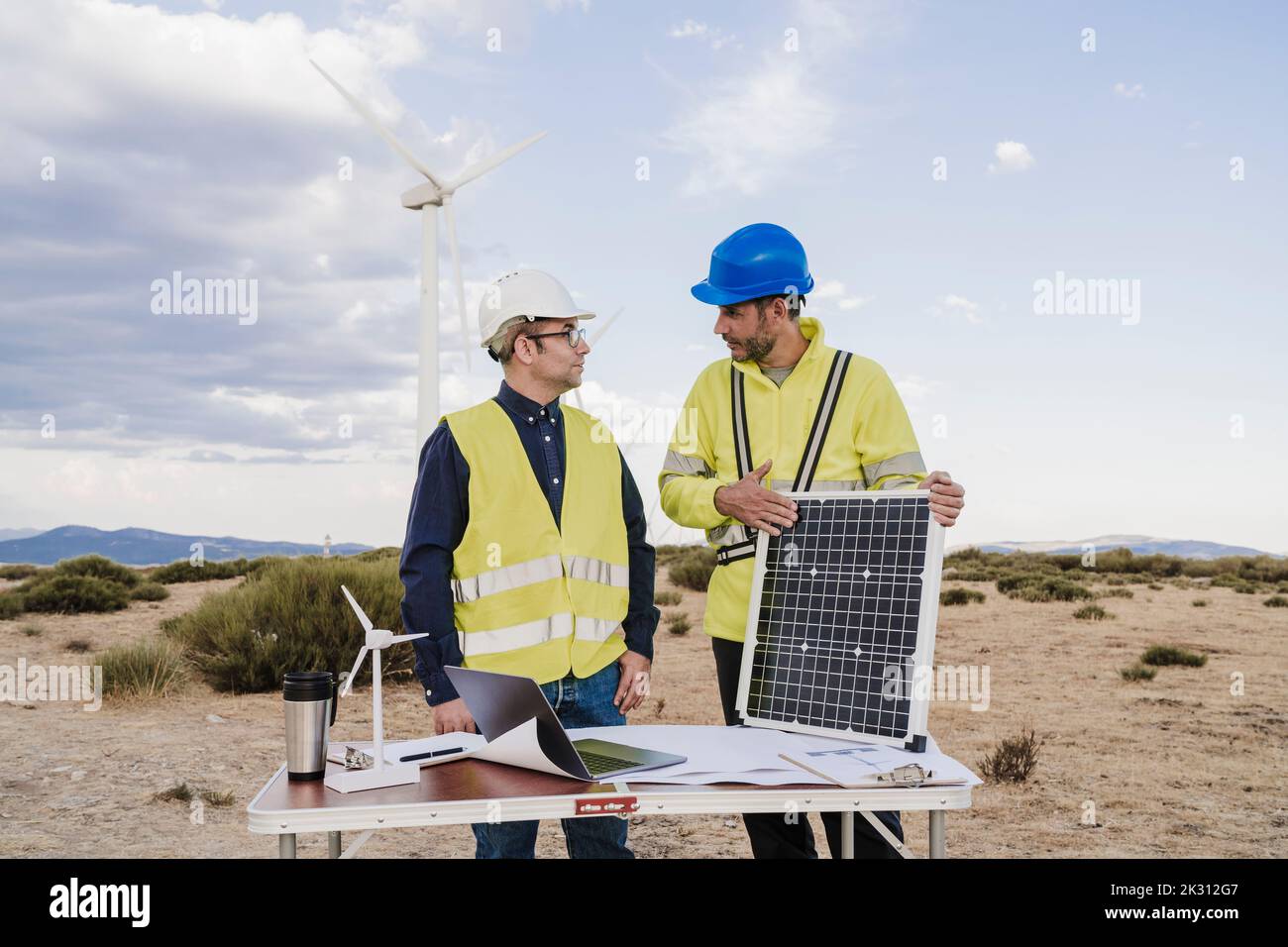 Ingegnere che tiene il pannello solare discutere con il collega alla scrivania presso la fattoria eolica Foto Stock