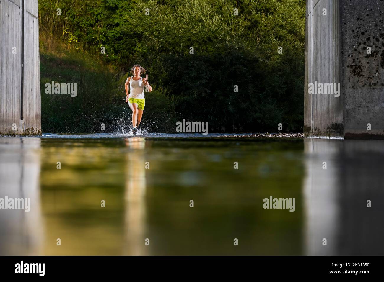 Giovane donna attiva che corre attraverso l'acqua Foto Stock