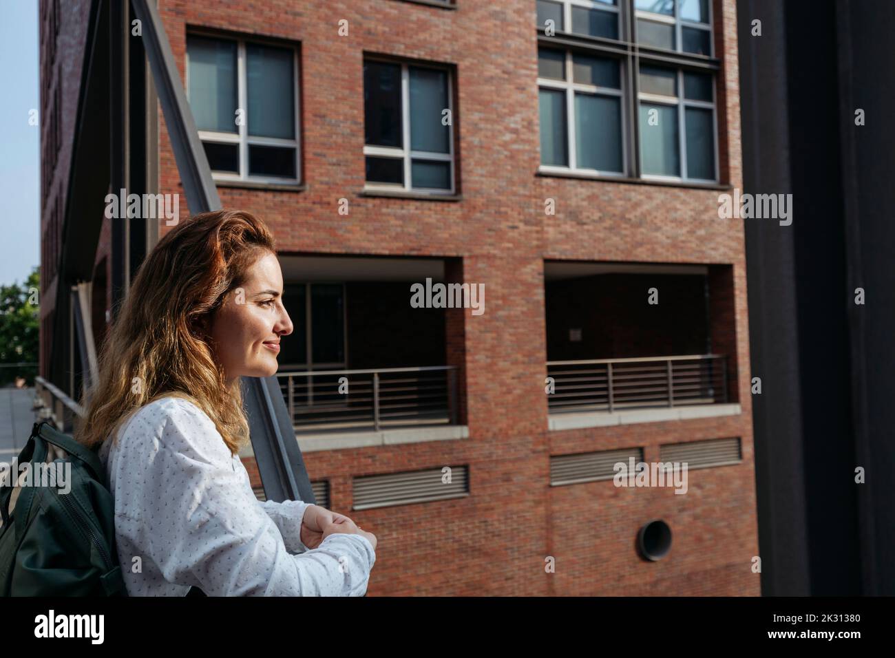 Donna sorridente in piedi accanto alla ringhiera di fronte all'edificio Foto Stock