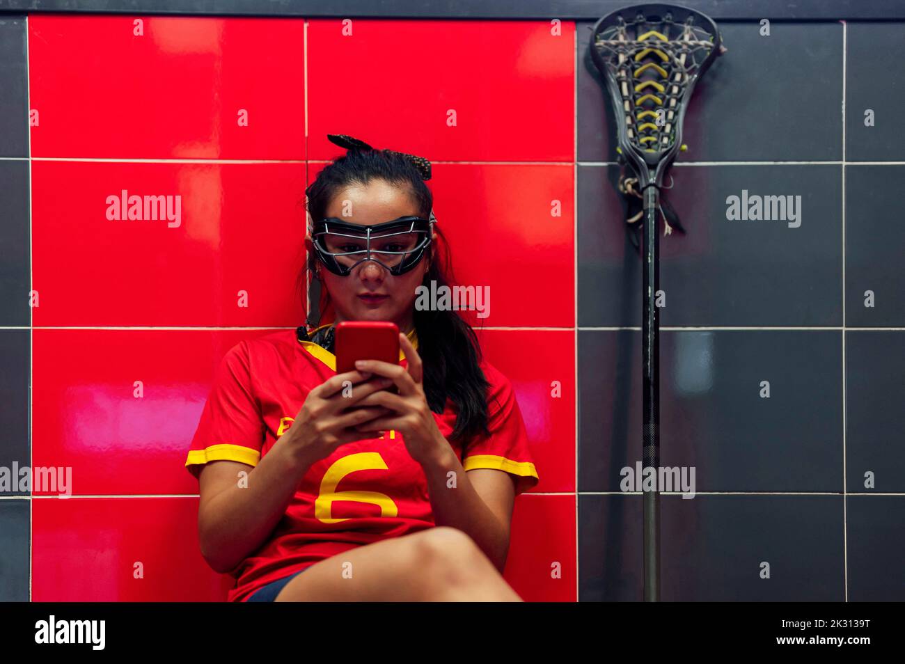 Messaggi di testo con lettore lacrosse utilizzando uno smartphone seduto nello spogliatoio Foto Stock