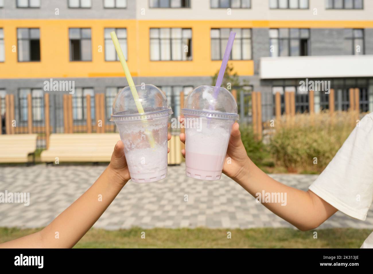 Mani di ragazze che tengono tazze usa e getta di milkshakes di fronte alla costruzione il giorno di sole Foto Stock