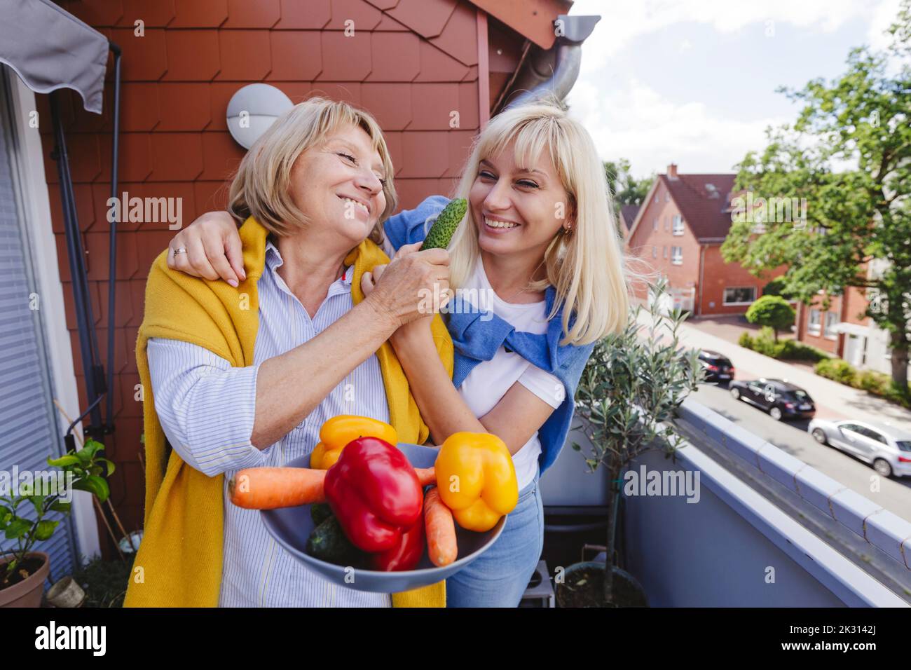 Donna felice con madre che tiene una ciotola di verdure fresche in piedi in balcone Foto Stock