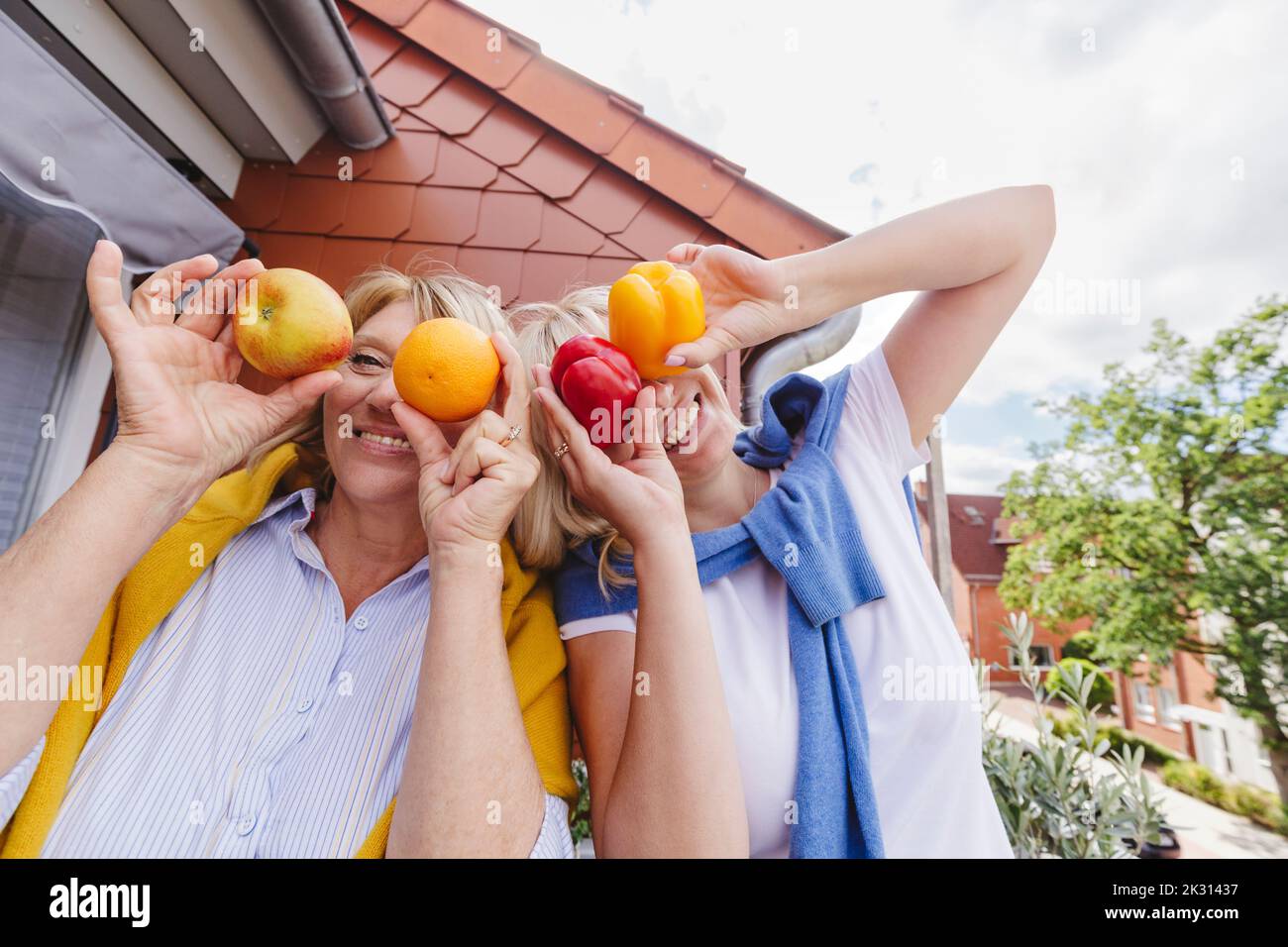 Madre felice con la figlia che tiene frutta e verdura sopra le facce Foto Stock