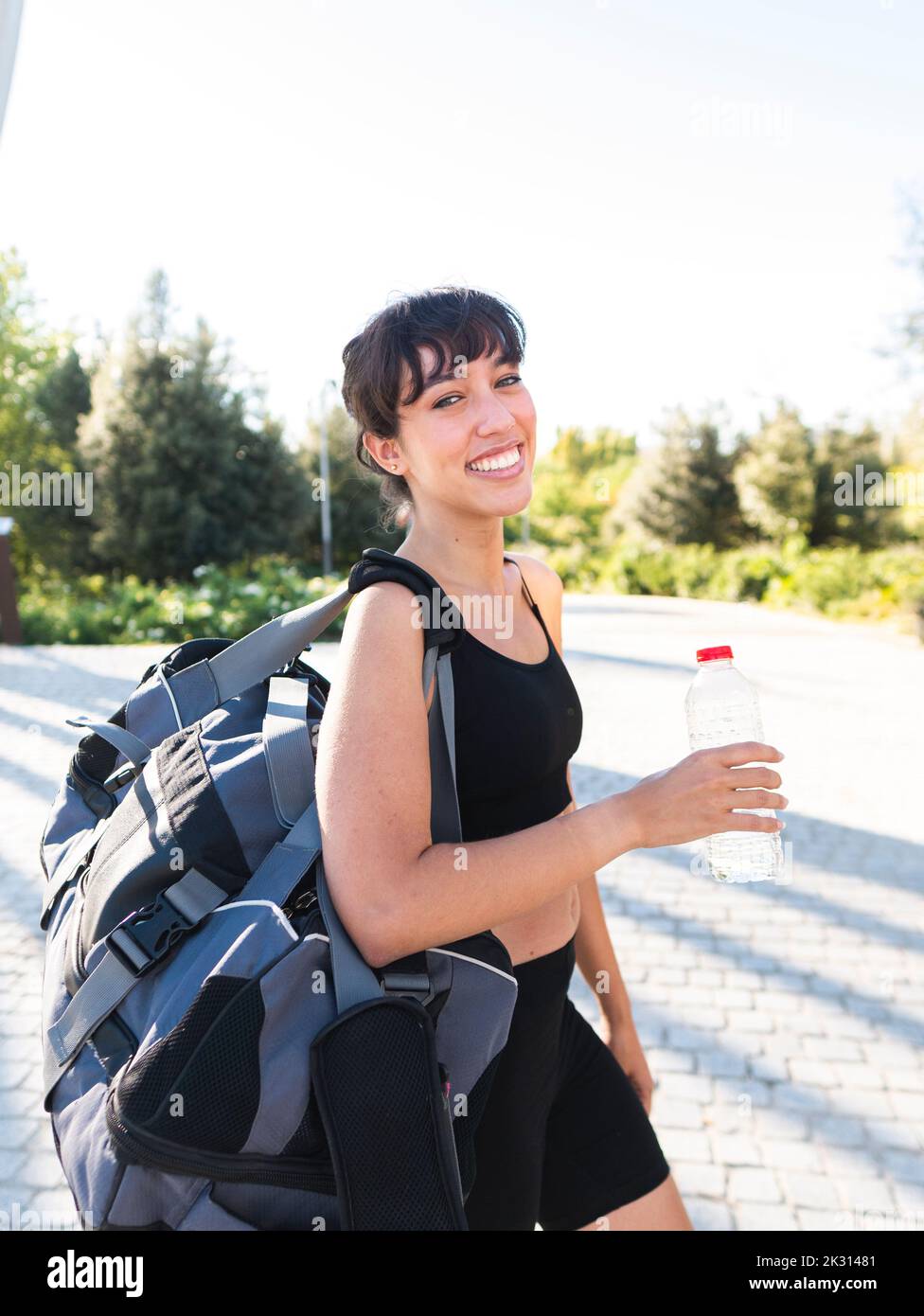 Donna felice con borsa palestra e bottiglia d'acqua a piedi Foto Stock