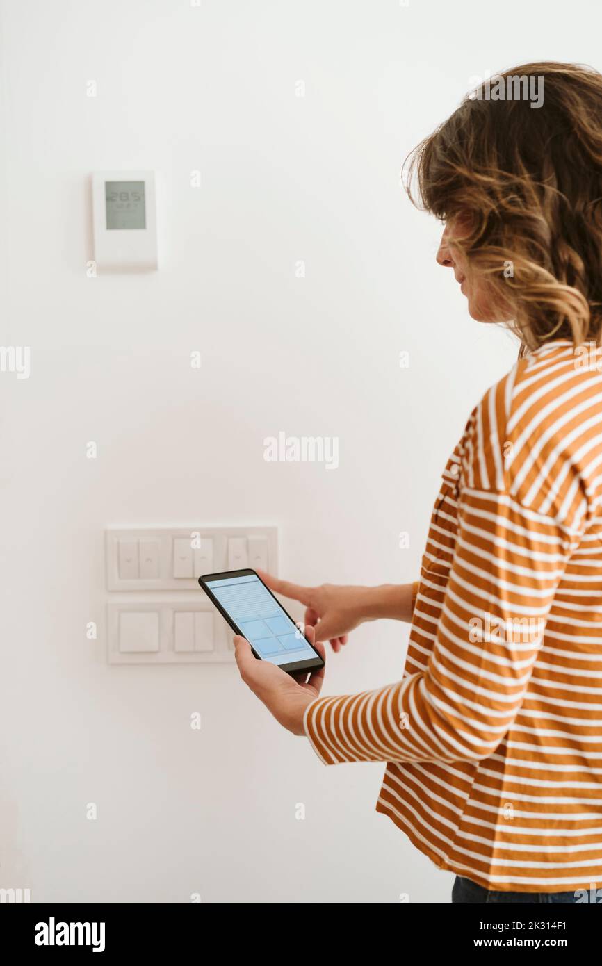 Giovane donna che tocca l'interruttore per i ciechi mentre controlla l'app del telefono cellulare Foto Stock