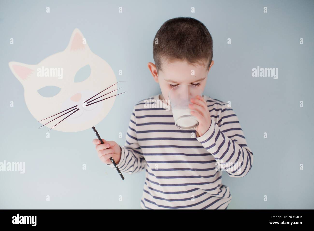 Ragazzo con maschera di Halloween che beve latte di fronte alla parete grigia Foto Stock