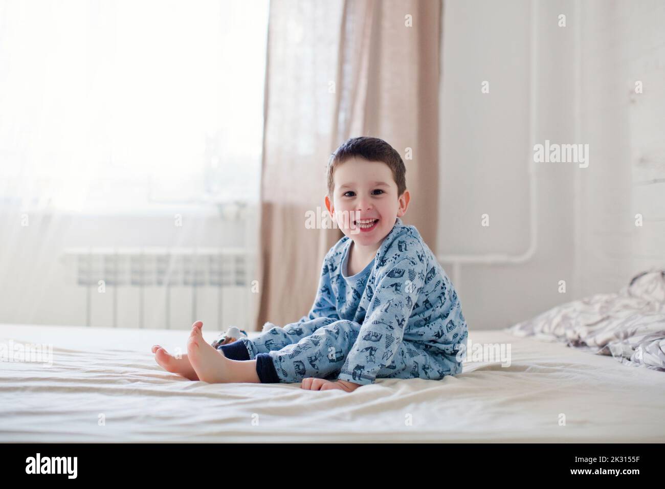 Felice ragazzo carino con pigiama seduto sul letto Foto Stock