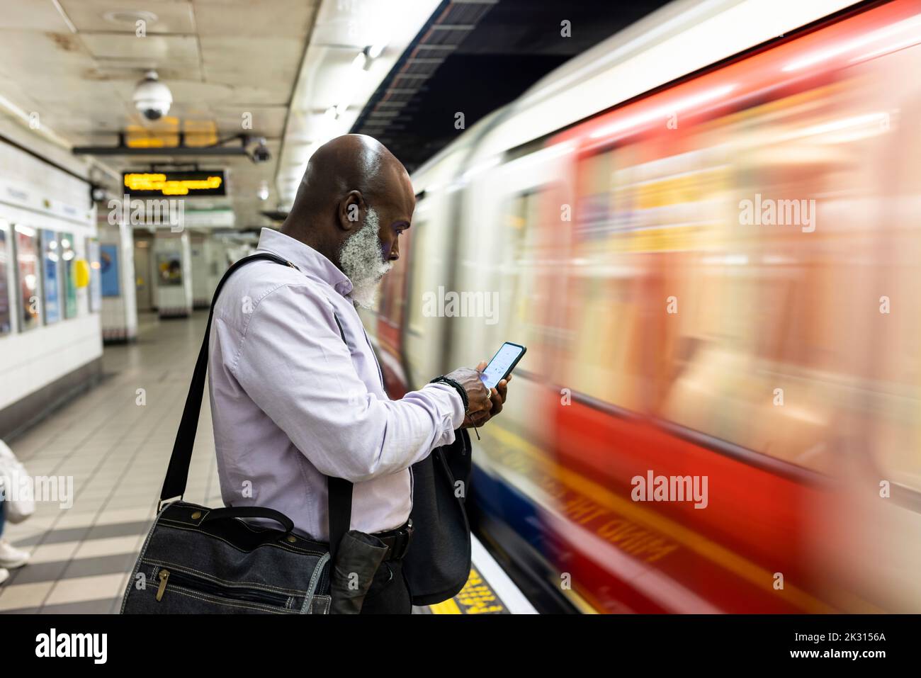 Uomo d'affari anziano calvo che usa lo smartphone vicino al treno veloce alla stazione Foto Stock