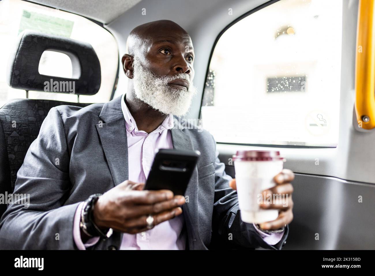Passeggero senior con smartphone con caffè in taxi Foto Stock