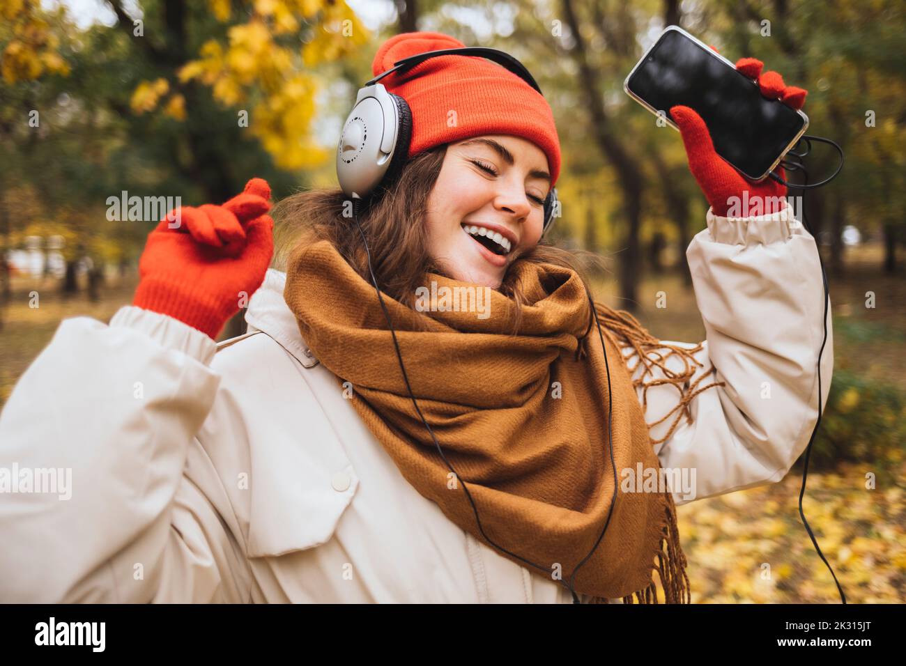 Donna con gli occhi chiusi che ascolta la musica attraverso le cuffie che ballano al parco Foto Stock
