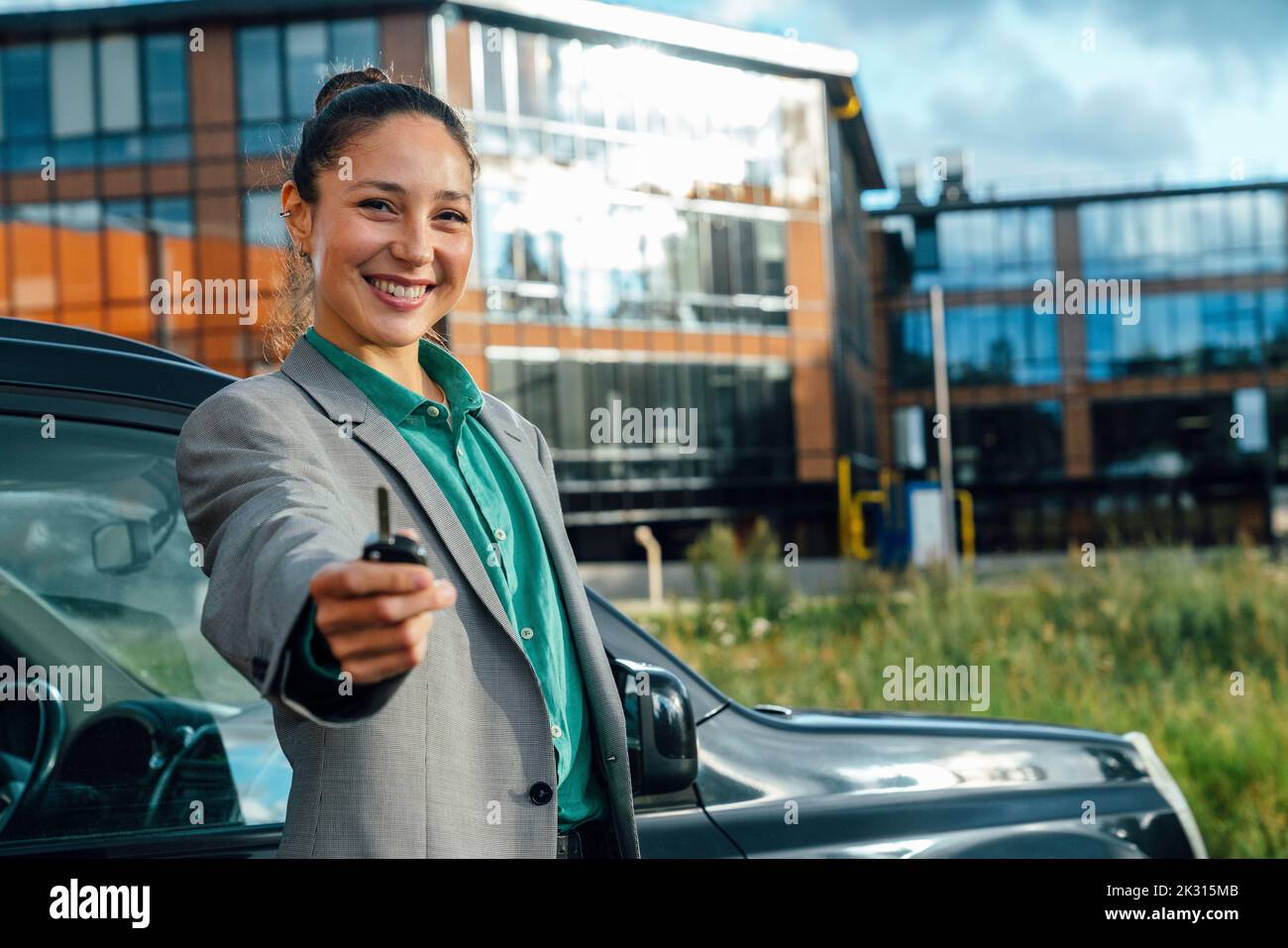 Donna d'affari con chiave e auto di fronte all'edificio degli uffici nelle giornate di sole Foto Stock