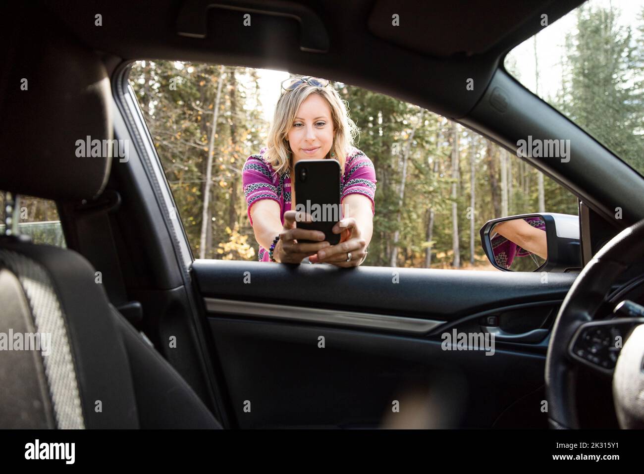 Donna che prende selfie visto dall'interno dell'auto Foto Stock