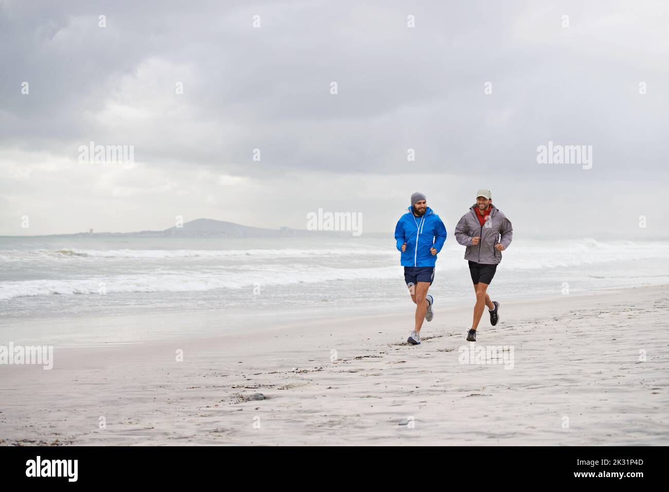 Mattina correre sulla spiaggia con un amico. Scatto a tutta lunghezza di due uomini che camminano insieme lungo la spiaggia in una mattinata piena. Foto Stock