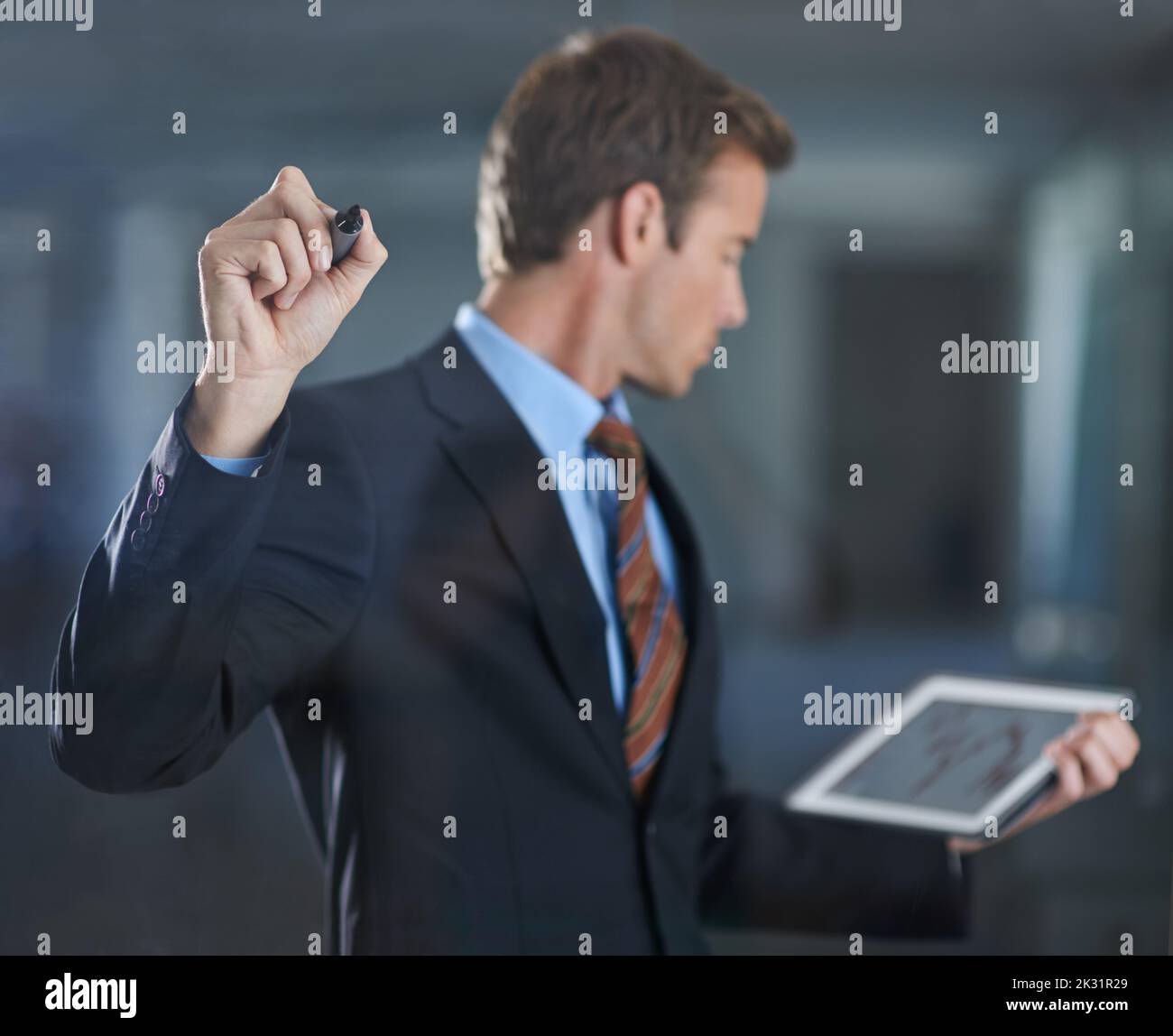 Tracciando il suo margine di profitto. Un bel giovane uomo d'affari che scrive sul vetro con un pennarello mentre tiene un tablet digitale. Foto Stock