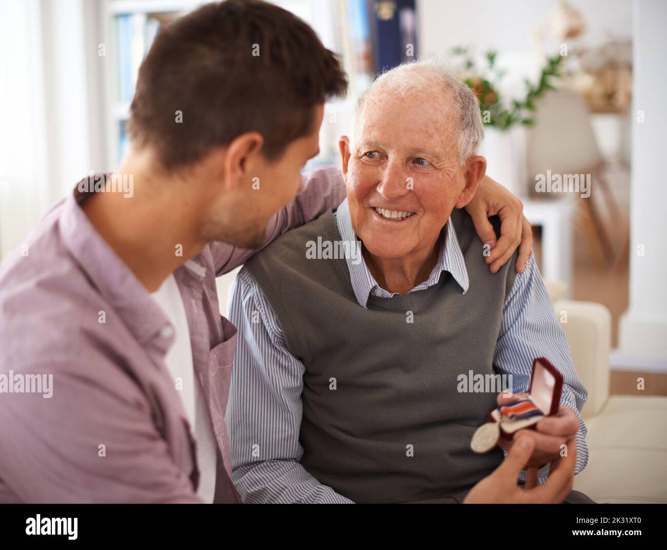 tradizioni di famiglia. un padre anziano che dà al figlio una medaglia mentre theyre si siede all'interno. Foto Stock