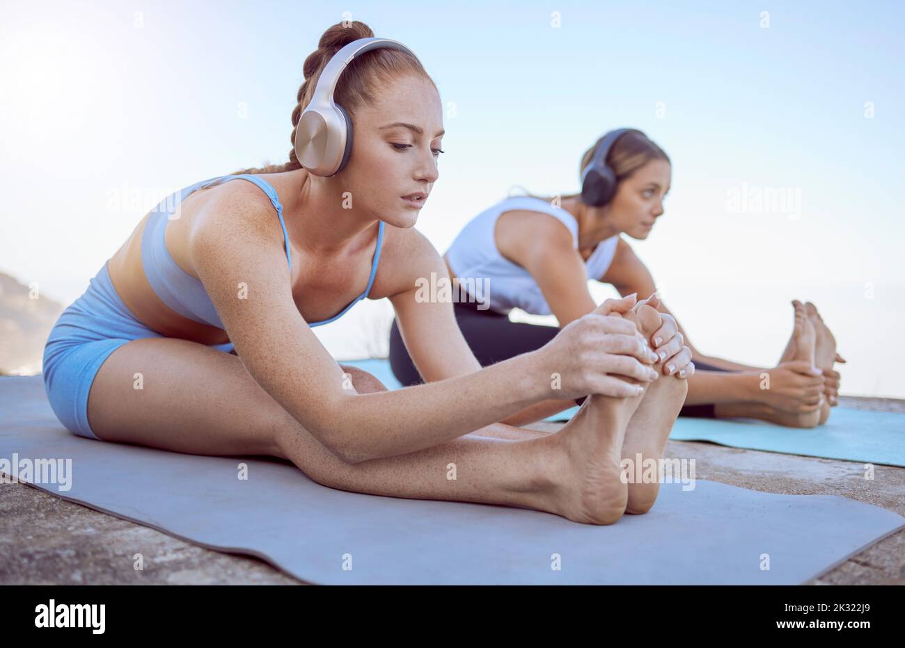 Cuffie, stretching e donne in spiaggia yoga per radio fitness, relax allenamento o zen esercizio in natura. Amici, persone o musica per pilates Foto Stock
