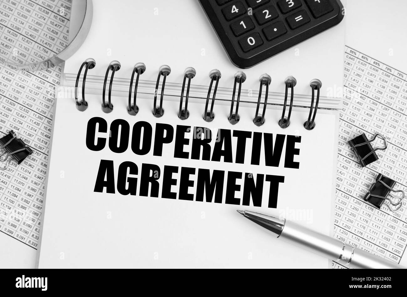 Concetto di business e finanza. Sulla tabella è riportata una lente d'ingrandimento, una calcolatrice e un quaderno con l'iscrizione - accordo cooperativo Foto Stock