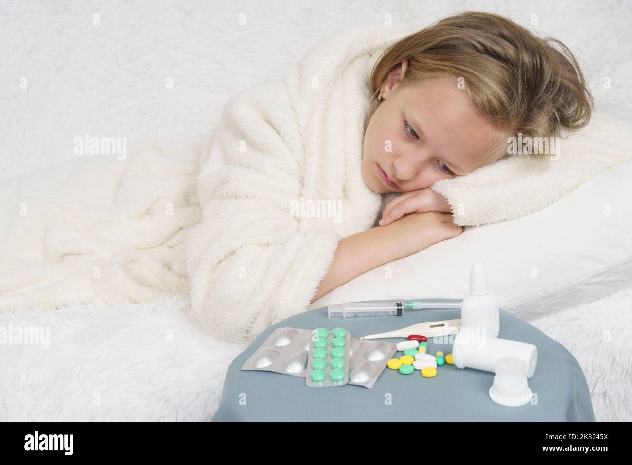 Una ragazza adolescente ammalata si trova sul letto e guarda la medicina. Concetto medico. Foto Stock