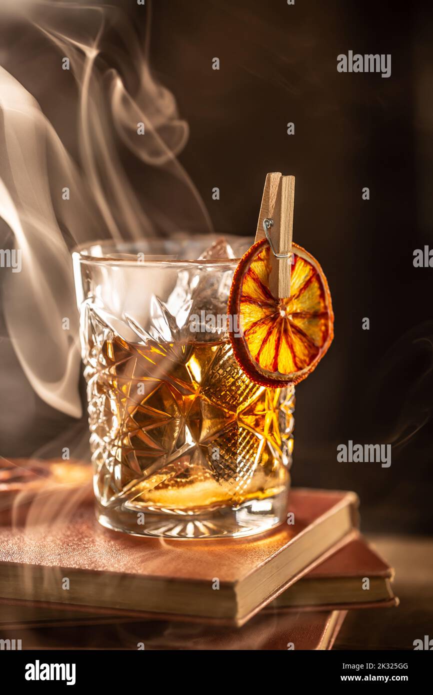 Cocktail al rum affumicato vecchio stile con cubetti di ghiaccio su sfondo scuro. Foto Stock