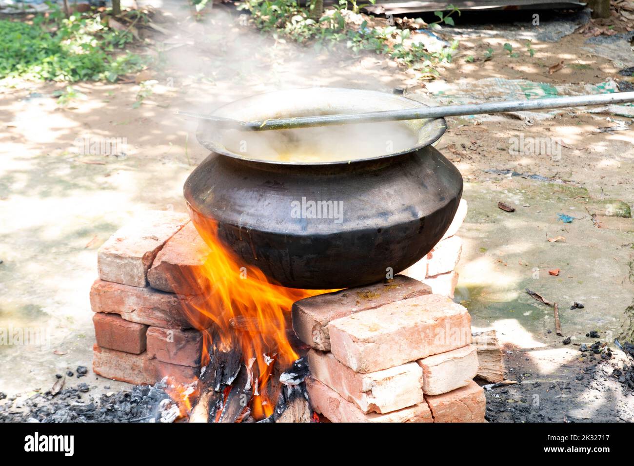 Biryani cucina in un villaggio festa su un forno temporaneo in mattoni. Cucina all'aperto per molte persone in una grande padella di alluminio con fuoco di legno. Foto Stock