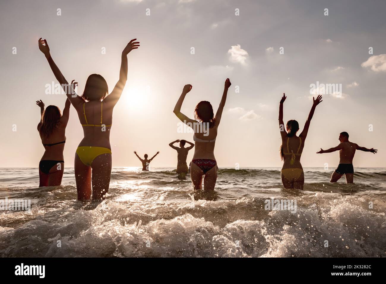 Un gruppo di giovani amici felici si rilassano al tramonto sulla spiaggia di mare. Concetto di vacanza tropicale Foto Stock