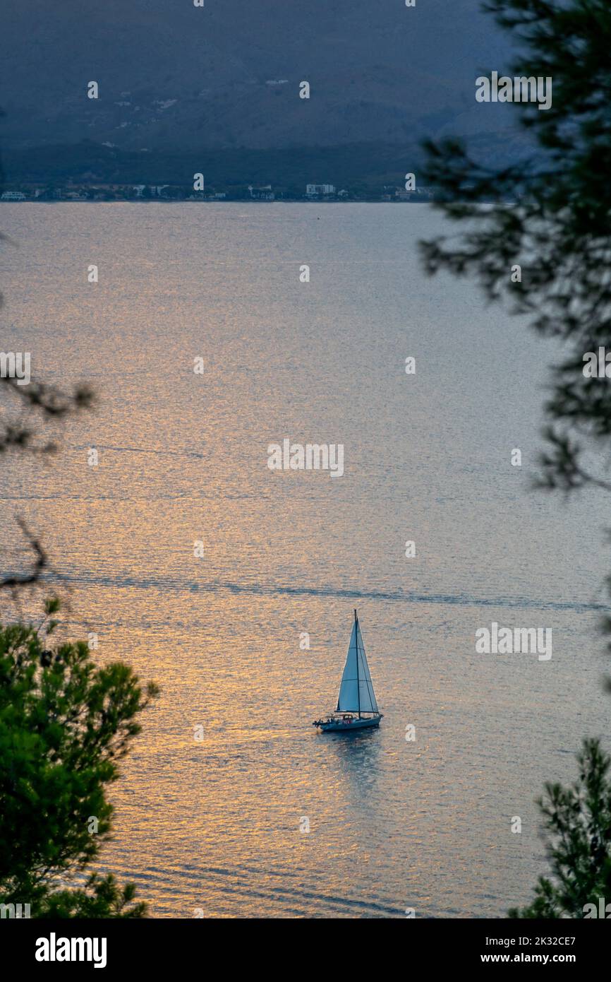 Vista in lontananza di una barca a vela nelle acque calme del Mar Mediterraneo a Maiorca (Spagna) al tramonto Foto Stock
