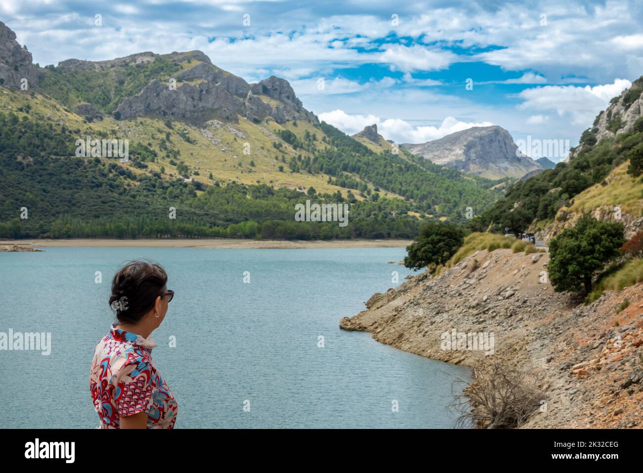 Donna di 50 anni con un abito fiorito e occhiali da sole che ammirano la bellezza del bacino di Gorg Blau a Maiorca (Spagna) una mattina d'estate Foto Stock