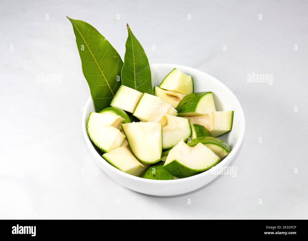 una ciotola di mango verde crudo con foglie di mango isolate su fondo bianco. Foto Stock