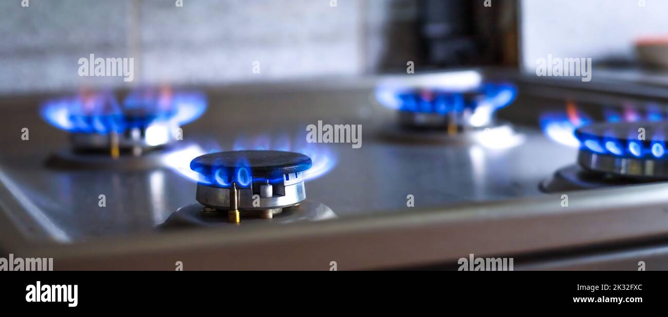 Primo piano di un fuoco blu da una stufa da cucina. 4 bruciatori a gas a fiamma viva. concetto economico. banner ampio Foto Stock