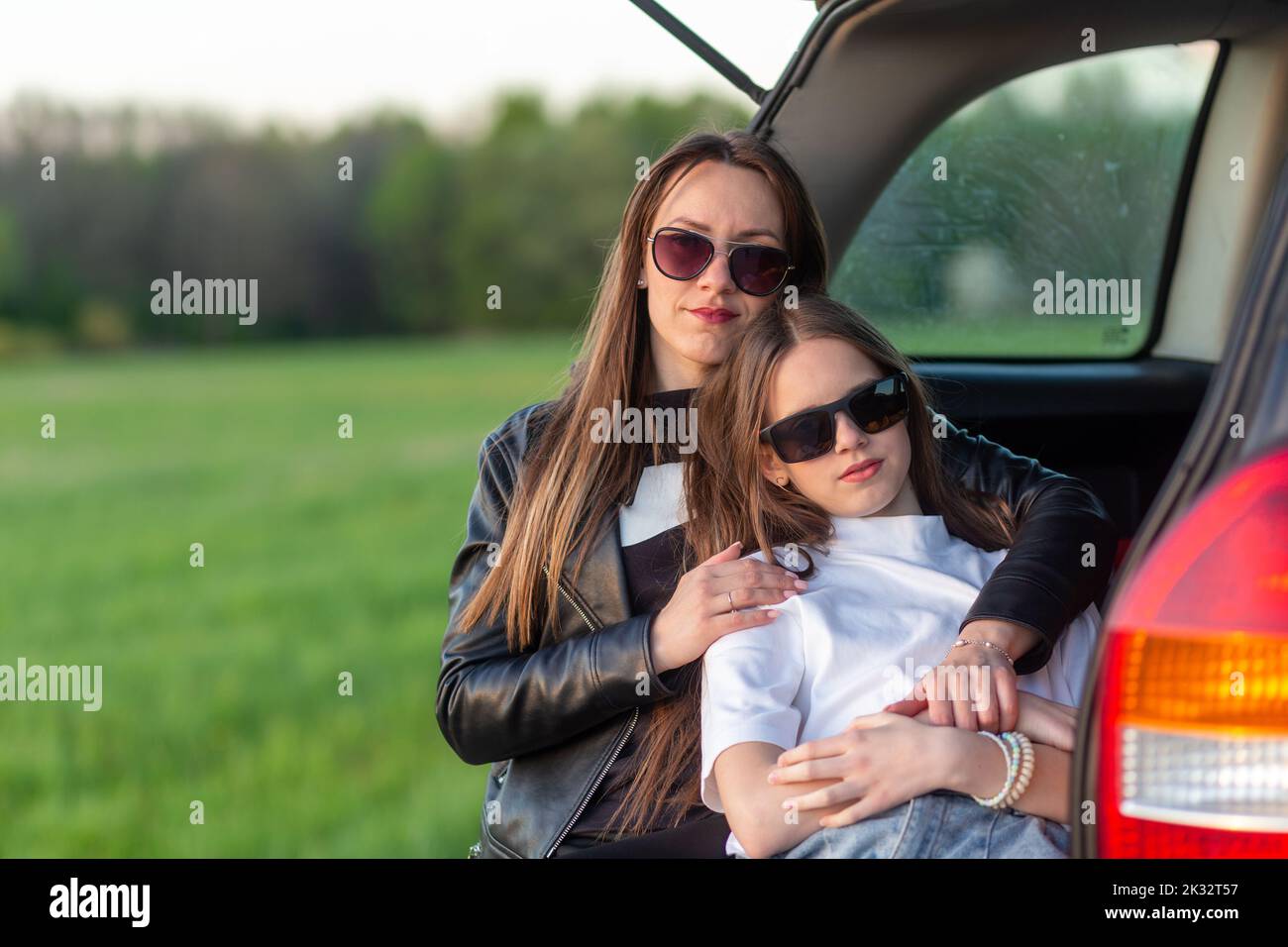 Madre e figlia si accampano su una collina e ammirano il tramonto mentre si siedono nel bagagliaio dell'auto Foto Stock