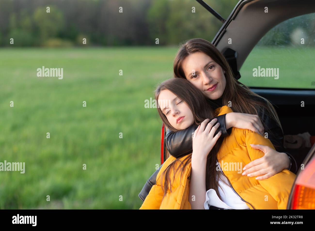 Madre e figlia si accampano su una collina e ammirano il tramonto mentre si siedono nel bagagliaio dell'auto Foto Stock