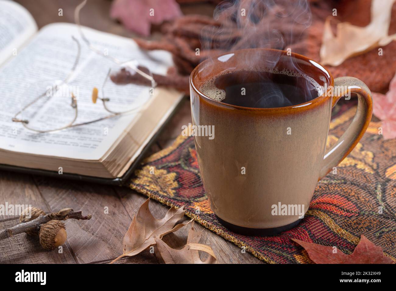 Tazza calda di caffè sul tappeto autunnale con libro e coperta sullo sfondo Foto Stock