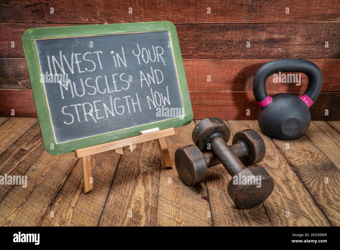 investi ora nei vostri muscoli e forza - testo motivazionale su una lavagna con i dumbbells ed il kettlebell, il concetto di salute e di idoneità Foto Stock