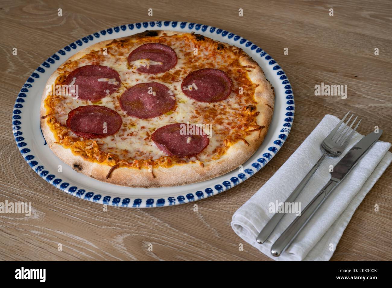 Pizza al Salame in stile italiano su un piatto rotondo con coltello e forchetta Foto Stock