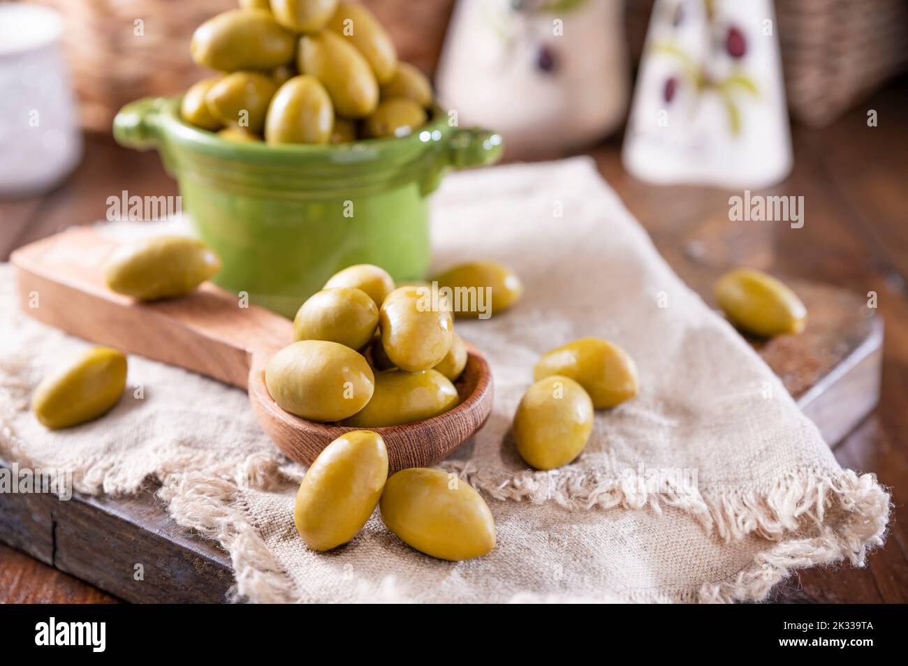 Grandi olive verdi in una tazza su un tavolo di legno. Olive italiane, vendemmia Sardenya e Grecia. L'olio d'oliva viene versato sulle bacche, le foglie d'oliva nel telaio. Primo piano. Copia sapce Foto Stock